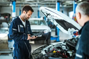 A person opening up the hood of a vehicle holding an onboard diagnostics (OBD) scanner