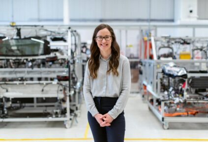 A picture of a smiling woman with engineering parts, presumably NDIR sensors, in the background on shelves