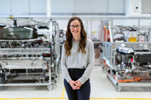 A picture of a smiling woman with engineering parts, presumably NDIR sensors, in the background on shelves